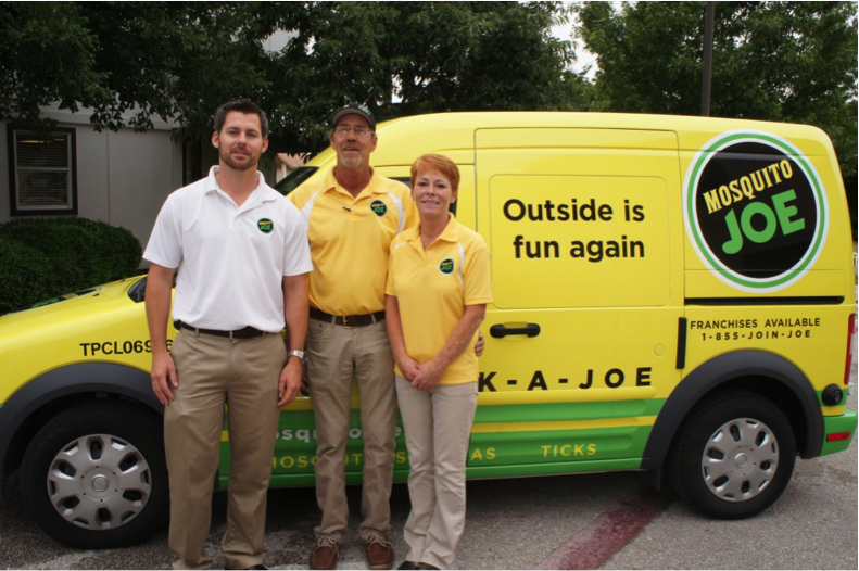 Mosquito Joe of Greater Austin team poses for a photo in front of a yellow and green service van.